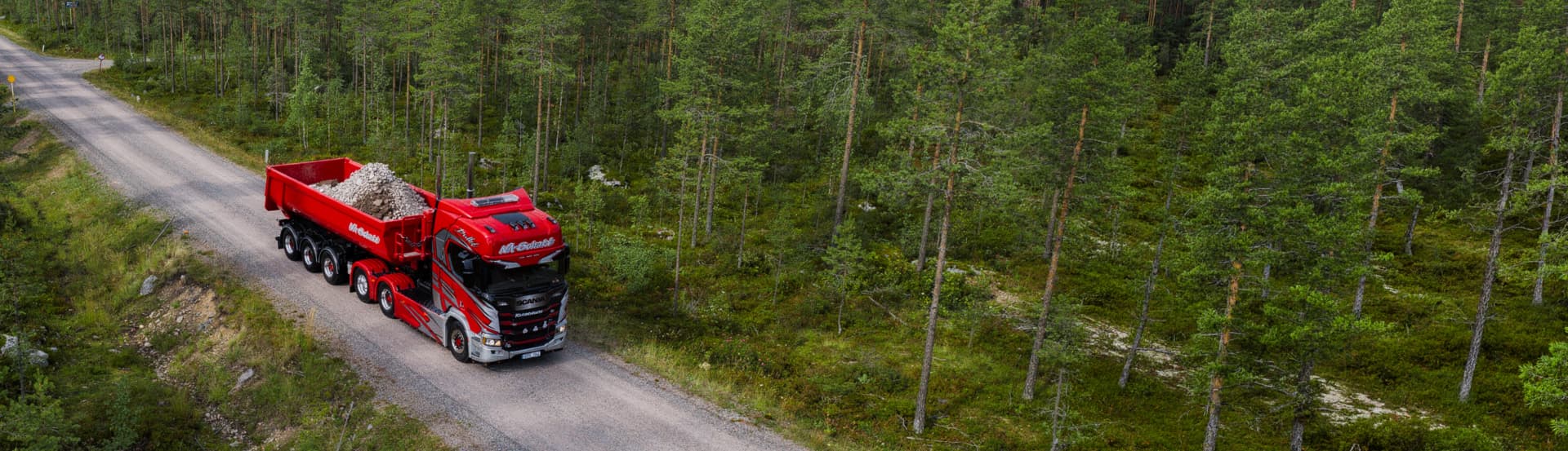 Röd lastbil med släp lastad med grus på en grusväg genom skogen
